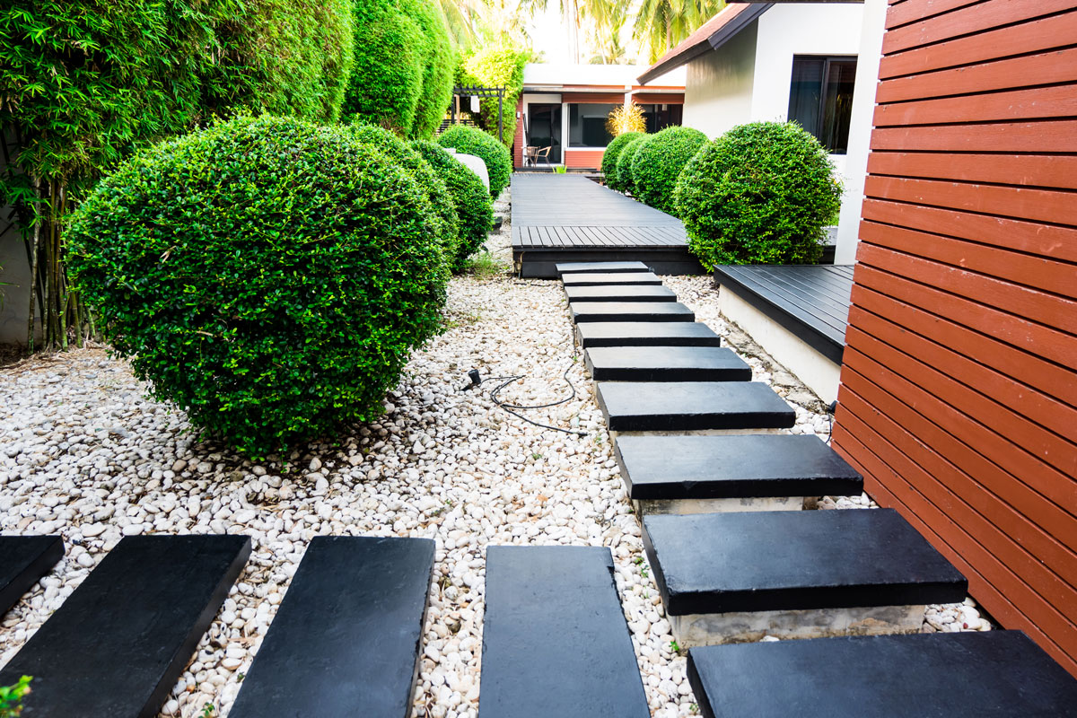 Štrkový chodník s čiernym nášľapnými kameňmi vedúci k terase moderného rodinného domu