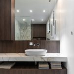 moderná kúpeľňa s obkladom v imitácii kameňa, s tmavým drevodekórom na skrinkách a veľkoplošným zrkadlom