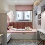 detská izba v kombinácii sivej, bielej a pastelovej ružovej s posteľou pod oknom, úložnými priestormi a s čalúnenými panelmi na stene po obvode postele