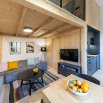moderný mezanínový interiér v kombinácii dreva a čiernej farby, s obývačkou a kuchyňou umiestnenou pod schodiskom