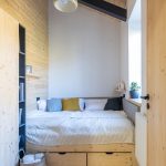 malá izba s dreveným obložením a posteľou na celú šírku miestnosti s úložnými priestormi pod posteľou