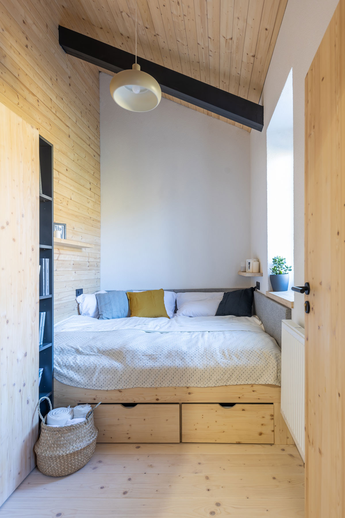malá izba s dreveným obložením a posteľou na celú šírku miestnosti s úložnými priestormi pod posteľou