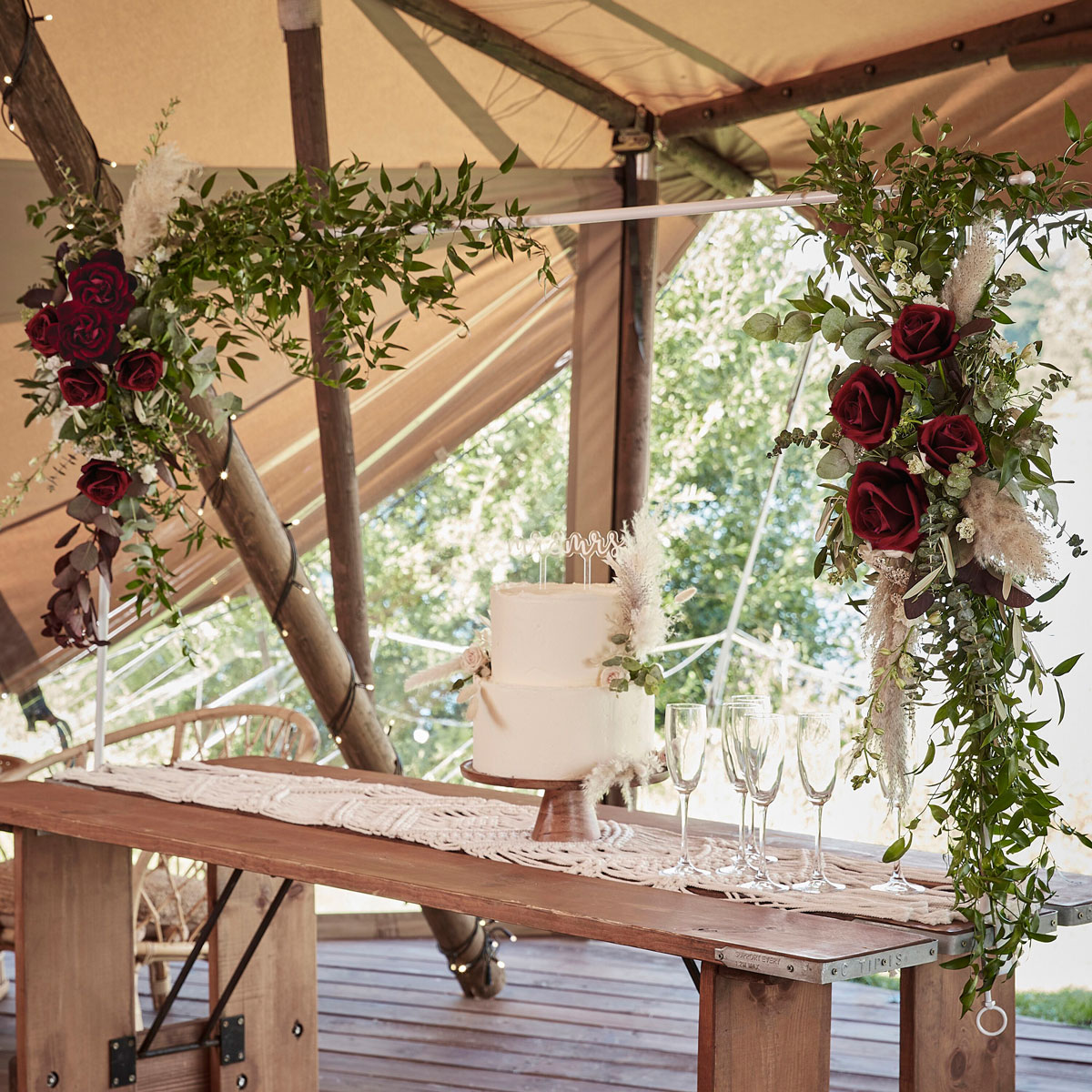 Drevený stôl so svadobnou tortou a aranžmánom z kvetín