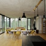 otvorený denný priestor obývačky s jedálňou so žltou sedačkou a stoličkami, s pohľadovým betónom na strope a celohliníkovými oknami s trojsklami