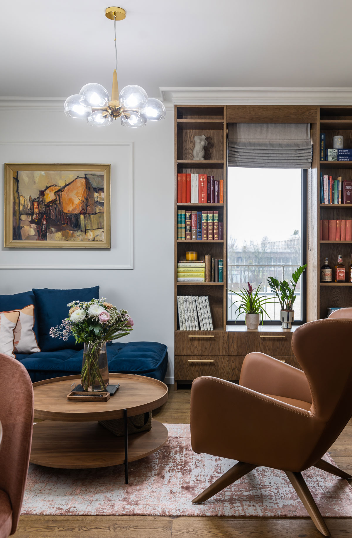 elegantná pánska obývačka s koženým ušiakom, tmavomodrou sedačkou a knižnicou z tmavého duba postavenou okolo okna