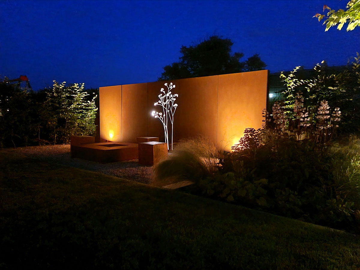 večerná okrasná záhrada s osvetlenou cortenovou stenou