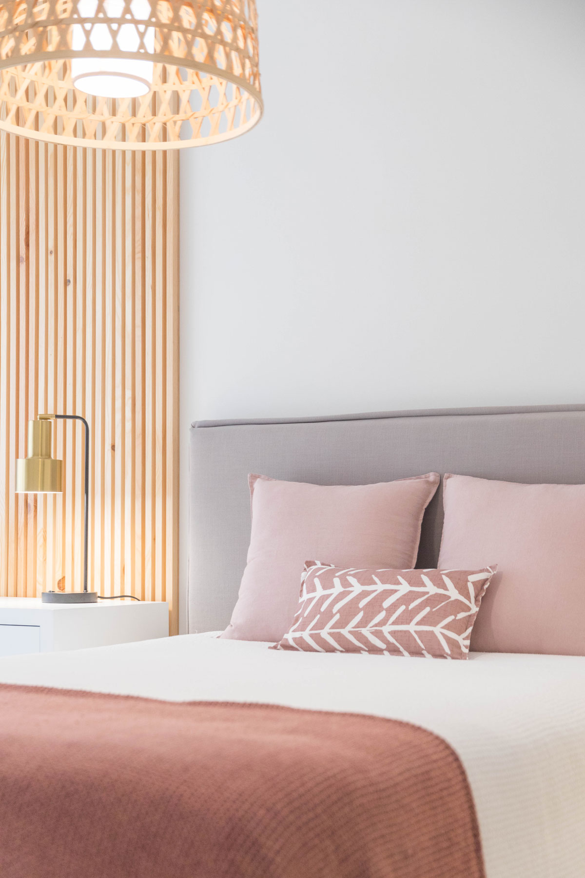 spálňa s posteľou v pastelových farbách, prírodnou lampou a dreveným obložením na stene